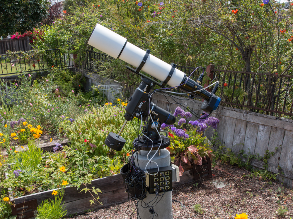My backyard astrophotography setup with my 130mm refractor telescope, mount and concrete pier. The sketchy fence in the background has since been replaced.